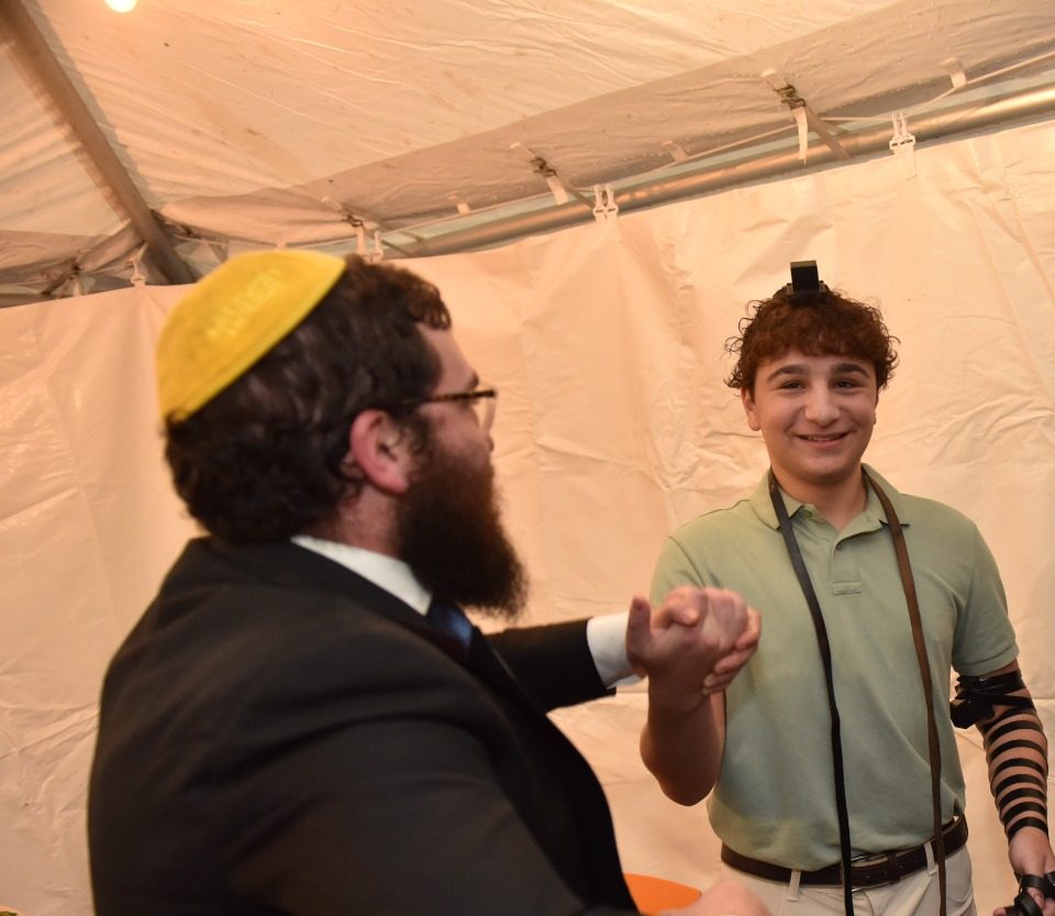 Rabbi Zalmy celebrating with a young man putting on tefillin